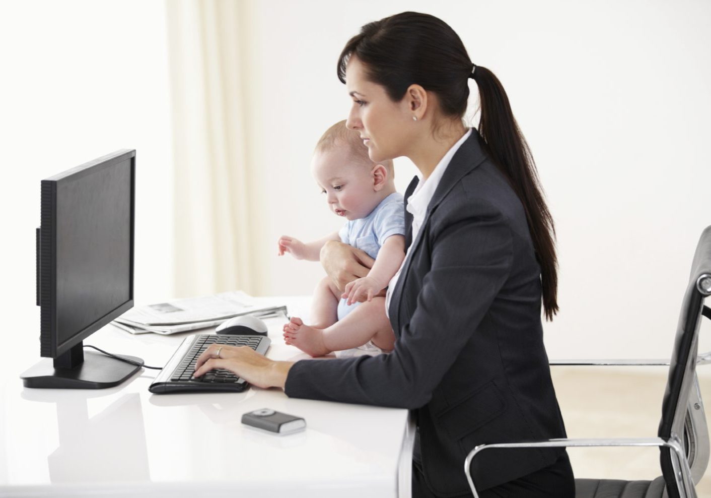 Working mother holding a baby while working on her computer - copyspace